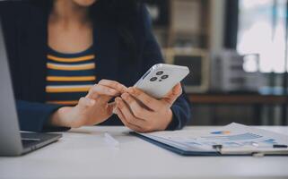 encantadora jovem empresária asiática sentada no computador laptop no escritório, fazendo o relatório calculando o documento de verificação do serviço de receita interna do saldo. foto