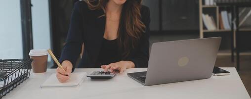 empresária asiática usando computador portátil e trabalhando no escritório com documento de calculadora na mesa, fazendo planejamento analisando o relatório financeiro, investimento em plano de negócios, conceito de análise financeira. foto