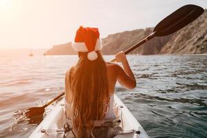 mulher dentro caiaque costas visualizar. feliz jovem mulher dentro santa chapéu flutuando dentro caiaque em calma mar. verão feriado período de férias e alegre fêmea pessoas relaxante tendo Diversão em a barco. foto