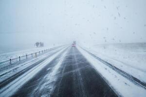 carro dirigindo em neve coberto rodovia estrada e nevasca com ventoso dentro campo às Islândia foto