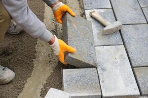 uma trabalhador deitado concreto tijolos em cada de outros para construção uma Novo calçada foto