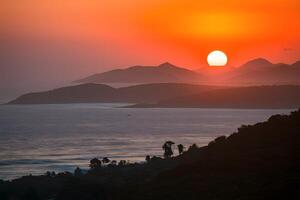 ai gerado laranja pôr do sol elencos caloroso brilho sobre oceano e montanha vista foto