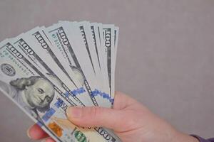 fêmea mãos segurando dólares notas em uma cinzento fundo. foto