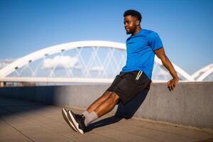 jovem afro-americano homem é exercício dentro a cidade. ele é fazendo marcha ré flexões. foto