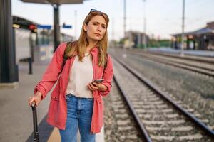 adulto mulher é em pé às estrada de ferro estação e esperando para chegada do trem. foto