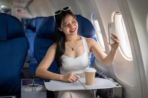 a atraente ásia fêmea passageiro é levando uma selfie com dela Smartphone durante a voo. foto