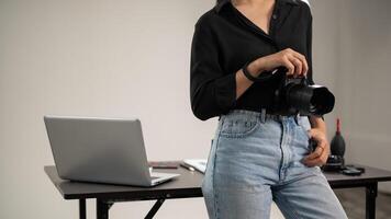 uma cortada tiro do uma fêmea fotógrafo é em pé dentro dela estúdio com uma dslr Câmera dentro dela mão. foto