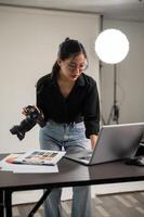uma profissional ásia fêmea fotógrafo é verificação imagens em dela computador portátil, trabalhando dentro uma estúdio. foto