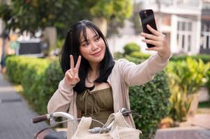 uma feliz ásia fêmea viajante é levando selfies enquanto explorando a cidade com dela bicicleta. foto