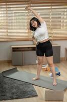 uma Forte ásia mulher dentro roupa de esporte é alongamento dela testemunho músculos e braços em uma ioga esteira. foto