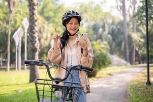 uma positivo ásia mulher é verificação uma mapa em dela Smartphone enquanto equitação uma bicicleta dentro uma verde parque. foto