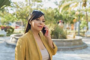 mulher falando em a telefone dentro uma público parque. ensolarado dia. foto