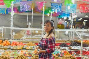 sorridente mulher com uma fervido milho Próximo para uma mercado ficar de pé dentro México. foto