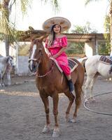 mexicano mulher vestindo tradicional vestir e charro chapéu em a cavalo. cinco de maionese celebração. foto