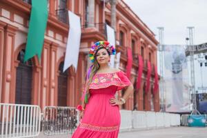 mexicano mulher vestindo tradicional vestir. rua decorado com cores do a mexicano bandeira. cinco de maionese celebração. foto