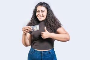 sorridente menina segurando uma 100 dólar conta gesticulando aprovado. jovem mulher segurando uma 100 dólar conta com polegar acima foto