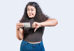 descontente jovem mulher segurando uma dólar conta com polegar baixa isolado. triste menina segurando uma uma 100 dólar conta com polegar baixa foto