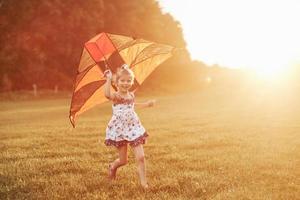 garota feliz correndo com a pipa na bela estação do ano sob o sol foto