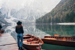 concepção turística. mulher de chapéu preto apreciando a paisagem montanhosa majestosa perto do lago com barcos foto