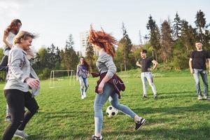 um grupo de amigos em trajes casuais joga futebol ao ar livre. as pessoas se divertem e se divertem. descanso ativo e pôr do sol panorâmico foto