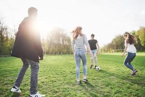 um grupo de amigos em trajes casuais joga futebol ao ar livre. as pessoas se divertem e se divertem. descanso ativo e pôr do sol panorâmico foto