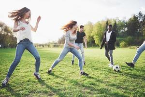 um grupo de amigos em trajes casuais joga futebol ao ar livre. as pessoas se divertem e se divertem. descanso ativo e pôr do sol panorâmico foto