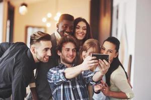 amigos se divertindo no restaurante. três meninos e três meninas fazendo selfie e rindo. no primeiro plano menino segurando o telefone inteligente. todos usam roupas casuais foto