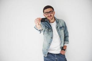 jovem bonito executivo masculino em traje casual, segurando um cartão de crédito nos bolsos em um fundo branco. o conceito de negociação na internet e a facilidade do dinheiro eletrônico foto