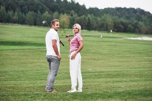 olhando para trás. dois jogadores de golfe com tacos nas mãos em pé no gramado foto