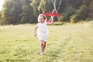 emoções sinceras. menina feliz correndo no campo com o avião de brinquedo vermelho nas mãos. árvores no fundo foto