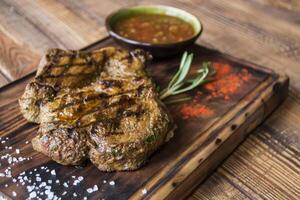 grelhado carne com molho e alecrim em uma de madeira mesa. foto