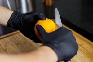 homem corte laranja descasca com Preto luvas japonês faca em de madeira corte borda foto