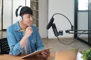 uma homem vestindo fones de ouvido é sentado às uma escrivaninha com uma computador portátil e uma caderno foto