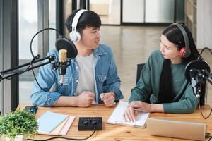 dois pessoas estão sentado às uma escrivaninha com microfones e uma computador portátil foto