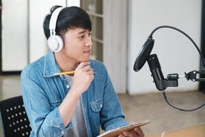 uma homem vestindo fones de ouvido e uma azul camisa é sentado às uma escrivaninha com uma lápis foto