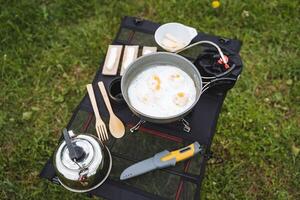 cozinhou Comida em uma caminhar é em a mesa, acampamento turista utensílios dentro natureza, Esmalte cozinhou em uma gás queimador, uma bushcraft faca. foto