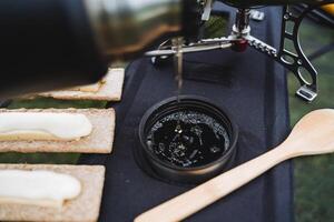 chá derrama para dentro uma caneca em topo do uma pão do água bolhas espuma Visão a partir de acima, uma quente beber a partir de uma garrafa térmica, acampamento comida, turista pratos. foto