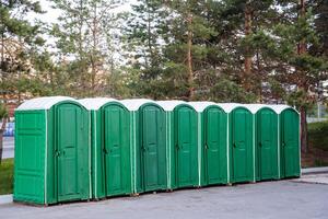 uma variedade do urbano cabines do compostagem banheiros, a ao ar livre banheiro do verde cor, uma plástico banheiro ecológico carrinhos em a asfalto, uma grupo do estandes. foto