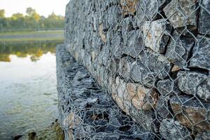 Rabitz malha detém a alvenaria, uma pilha do pedras é derramado para dentro uma cesta do arame, proteção do a costa a partir de destruição, fio tecelagem tecnologia foto