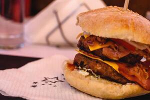 Duplo hamburguer com Duplo carne ou frango hambúrguer, tomate, cebola, alface, queijo, bacon e molho servido em Preto prato em branco fundo dentro grego taberna. Mediterrâneo cozinha. seletivo suave foco foto