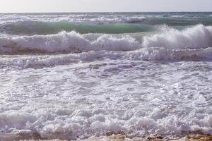 Forte ondas, salpicos e espuma falhando e espirrando em pedras em uma ensolarado dia. idílico marinha conceito. natureza, ambiente, ecologia temas. rude mar em costa mega limnionas, quios, Grécia. foto