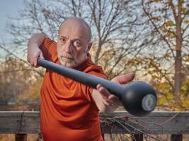 Senior homem é exercício com uma aço maça foto