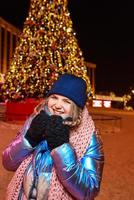 feliz sorridente jovem caucasiana no lenço, chapéu, jaqueta, luvas perto da árvore de Natal ao ar livre. ano novo, diversão, conceito de inverno foto