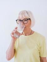 sênior mulher segurando um copo de água e água potável. estilo de vida saudável, esporte, conceito anti-idade foto