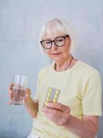 mulher sênior em copos segurando um remédio e um copo de água. idade, cuidados de saúde, conceito de tratamento