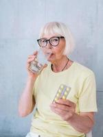 mulher sênior em copos segurando um remédio e um copo de água. idade, cuidados de saúde, conceito de tratamento