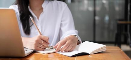 foto cortada mão de mulher escrevendo fazendo lista fazendo anotações no bloco de notas trabalhando ou aprendendo online com laptop em casa