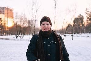 mulher sênior com chapéu e jaqueta esportiva, correndo no parque de inverno de neve. inverno, idade, esporte, atividade, conceito de temporada foto