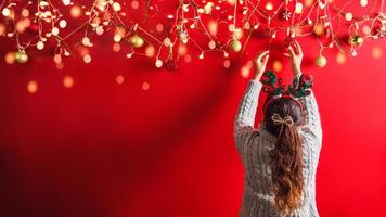 Feliz Natal e Feliz Ano Novo. A garota está projetando com decoração de enfeites de férias. o fundo de natal vermelho. com espaço de cópia para o seu texto. luzes LED foto