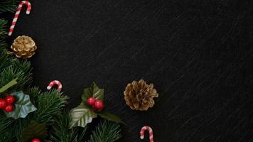 vista superior decorações de natal, folhas de pinheiro, bastão de doces e frutas vermelhas em plano de fundo texturizado preto escuro foto